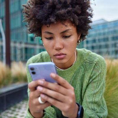 Personne regardant son smartphone assise à l’extérieur dans un environnement urbain moderne.