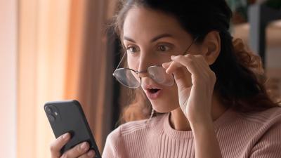 A woman appears surprised as she gazes at her smartphone screen, captivated by unexpected information or an astonishing revelation.