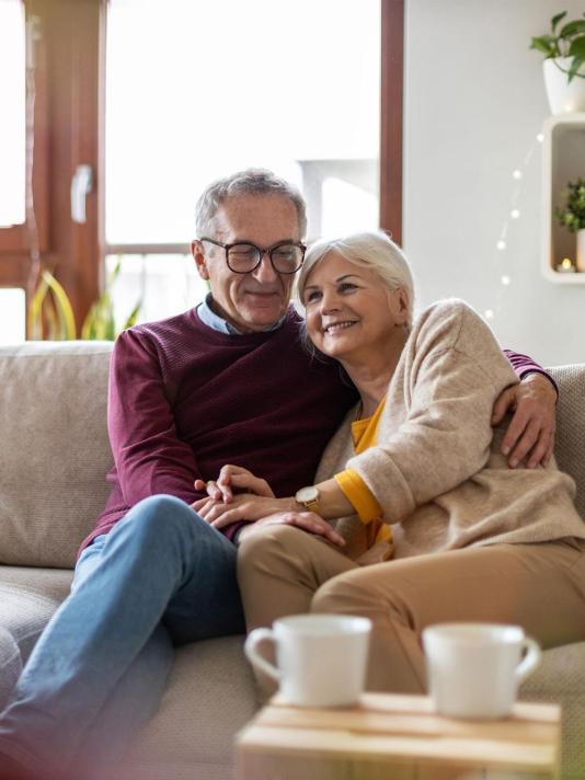 Happy elderly couple embraces each other while sitting on a couch.