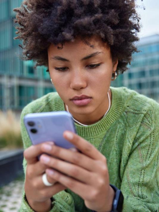 Personne regardant son smartphone assise à l’extérieur dans un environnement urbain moderne.