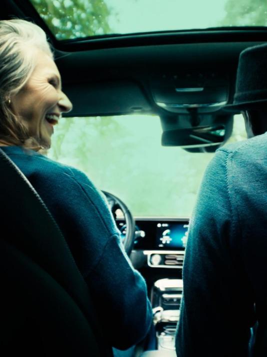  An elderly couple shares smiles and glances at each other as they enjoy a trip together, cruising in their car and cherishing the moments of companionship.