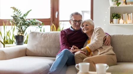 Happy elderly couple embraces each other while sitting on a couch.