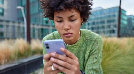 Personne regardant son smartphone assise à l’extérieur dans un environnement urbain moderne.